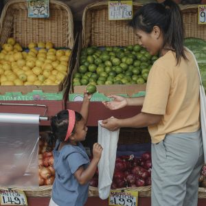 Back view Asian woman with daughter wearing casual outfits standing near local street market stall and choosing fruits