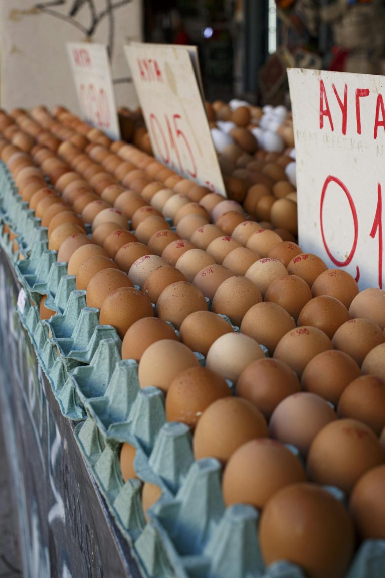 Rows of fresh brown eggs in blue cartons with Greek price signs at a local market.